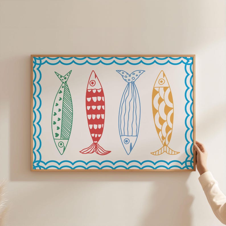 May include: A framed print with a white background and a blue wave border. Four colorful fish are depicted in the center of the print. The fish are green, red, blue, and yellow with different patterns.