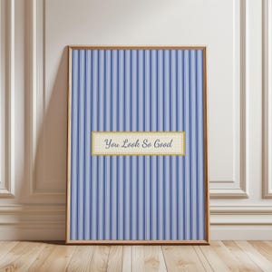 May include: A framed print with a blue and white striped background. A rectangular banner with the text "You Look So Good" is centered on the print. The frame is a light brown color.