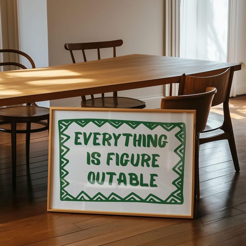 Pu&ograve; includere: Un cartello bianco incorniciato con la scritta "EVERYTHING IS FIGURE OUTABLE" in lettere verdi. Il cartello &egrave; in una cornice di legno marrone chiaro. Il cartello &egrave; su un pavimento di legno, con un tavolo e sedie di legno sullo sfondo.