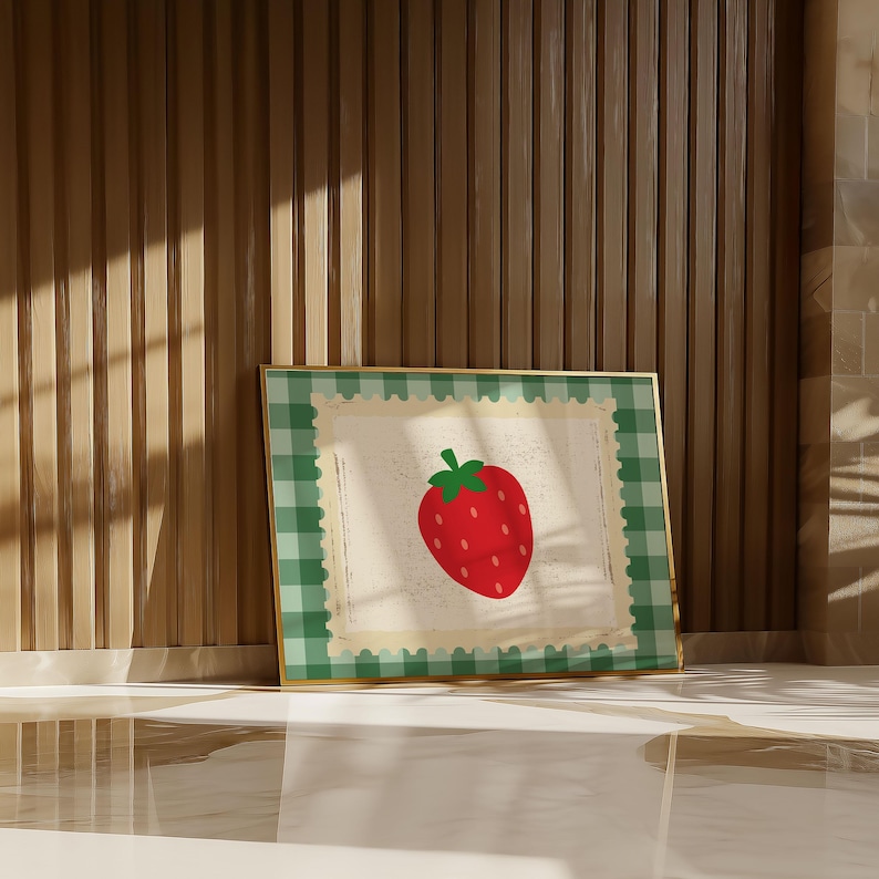 Puede incluir: Una impresi&oacute;n enmarcada con una fresa roja con hojas verdes. La obra de arte tiene un borde a cuadros verde y blanco y un marco dorado. El fondo es de color beige claro.