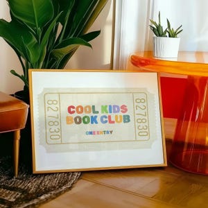 May include: A framed print with a gold border featuring a ticket design. The text "COOL KIDS BOOK CLUB" is displayed in colorful letters. The print includes the text "ONE ENTRY" and ticket numbers.