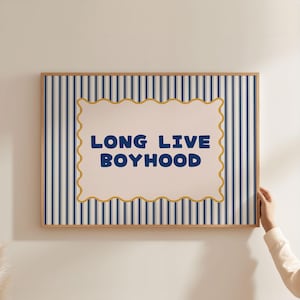 Puede incluir: Un estampado enmarcado con el texto "LONG LIVE BOYHOOD" en letras azules. El fondo presenta rayas verticales azul marino sobre un fondo blanco. El texto está dentro de un borde crema festoneado.