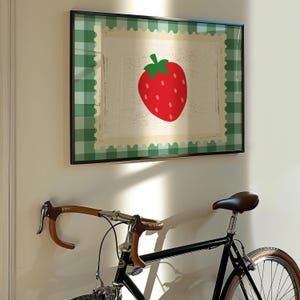 Puede incluir: Una impresi&oacute;n enmarcada con una gran fresa roja con hojas verdes. La obra de arte tiene un fondo crema con un borde festoneado y un borde a cuadros verde. Una bicicleta negra est&aacute; debajo.