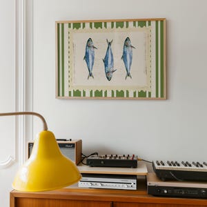 May include: A framed print of three blue fish with white stripes, hanging on a white wall. The frame has a green and white striped border.
