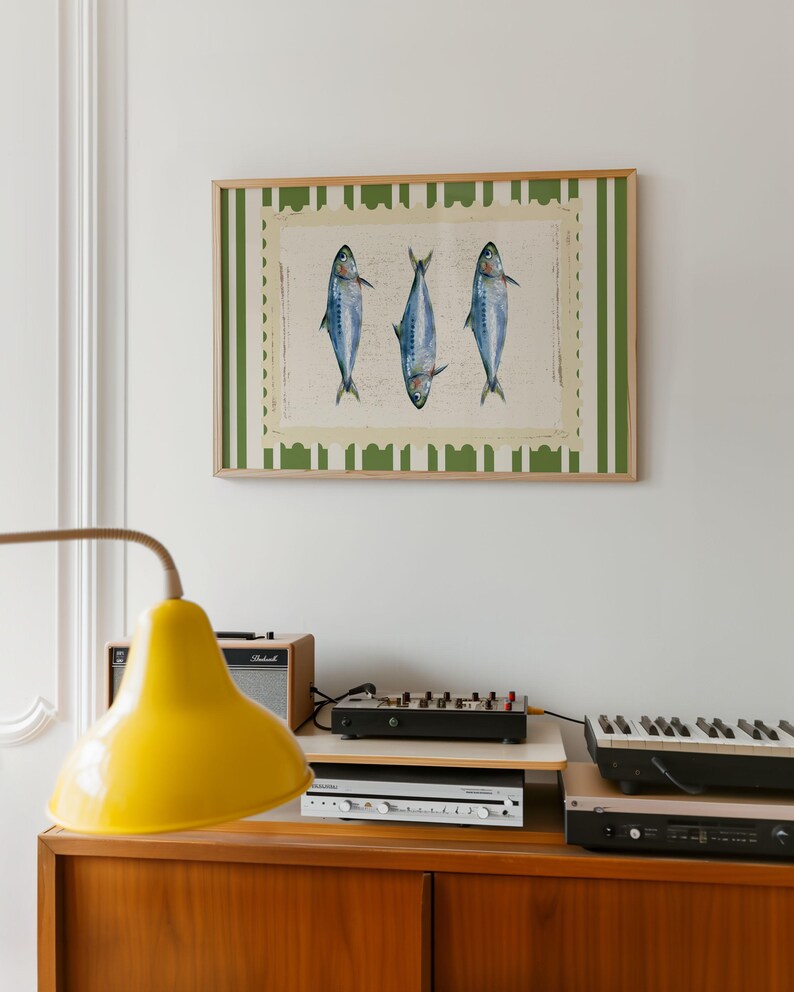 May include: A framed print of three blue fish with white stripes, hanging on a white wall. The frame has a green and white striped border.