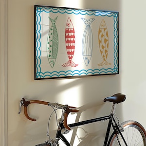 May include: A framed print of four colorful fish with a blue and white wave pattern border. The print is hanging on a white wall next to a black bicycle.