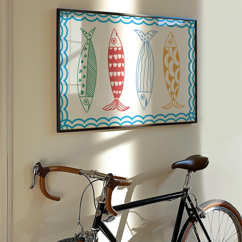 May include: A framed print of four colorful fish with a blue and white wave pattern border. The print is hanging on a white wall next to a black bicycle.