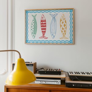 May include: A framed print of four colorful fish with different patterns. The fish are arranged in a row and are set against a white background. The frame is made of wood and has a light brown finish.