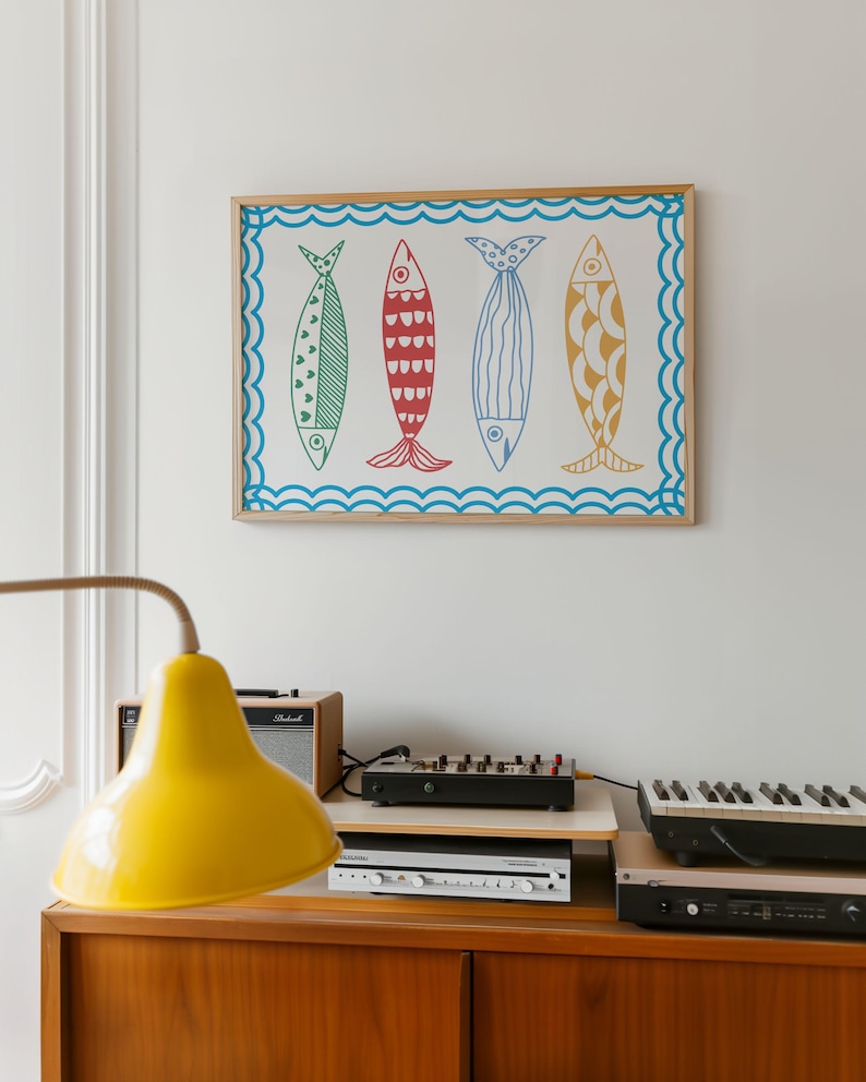 May include: A framed print of four colorful fish with different patterns. The fish are arranged in a row and are set against a white background. The frame is made of wood and has a light brown finish.