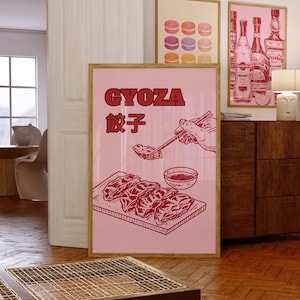 以下が含まれることがあります： ピンクのポスターに赤い文字で「GYOZA 餃子」と書かれている。ポスターには、箸を持った手が小さなソースのボウルに餃子を浸けている様子が描かれている。木製のまな板の上に餃子の皿が置かれている。