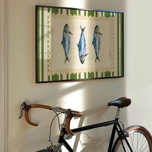 May include: A framed print of three blue fish on a white background with a green and white striped border. The print is hanging on a white wall next to a black bicycle with brown handlebars.