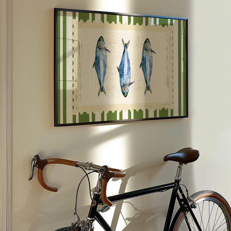 May include: A framed print of three blue fish on a white background with a green and white striped border. The print is hanging on a white wall next to a black bicycle with brown handlebars.