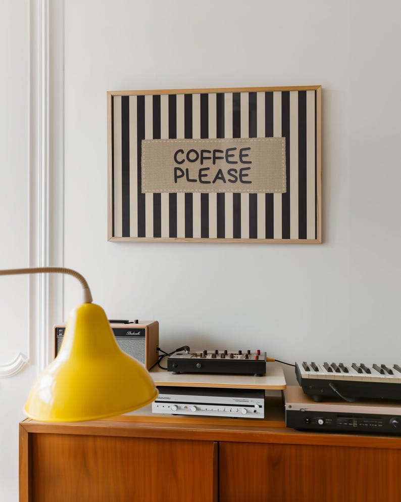 Puede incluir: Una obra de arte enmarcada con rayas verticales en blanco y negro y el texto "COFFEE PLEASE" en un parche beige. Una l&aacute;mpara amarilla, equipo de audio y un teclado se encuentran sobre un mueble de madera.