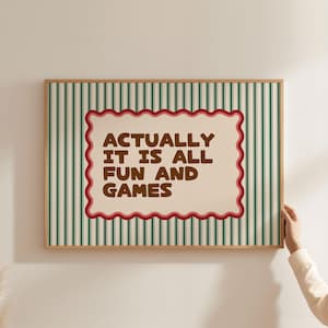 Può includere: Una stampa incorniciata con sfondo color crema e strisce verticali verdi. La stampa presenta un rettangolo color crema con bordi smerlati con il testo "ACTUALLY IT IS ALL FUN AND GAMES" in lettere marroni.