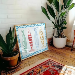 May include: A framed print of four colorful fish with a blue, white, and red pattern. The fish are set against a white background with blue waves. The frame is gold.