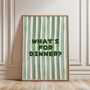May include: A framed print featuring a watercolour design of vertical green and white stripes. The text "WHAT'S FOR DINNER?" is in bold green letters. The frame is a light brown colour.