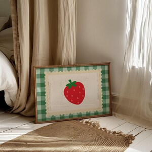 Puede incluir: Una impresi&oacute;n enmarcada con una fresa roja con tallo y semillas verdes. La obra de arte est&aacute; sobre un fondo blanco con un borde tipo sello postal, enmarcado por un patr&oacute;n de cuadros verdes y blancos. El marco es de color madera natural.