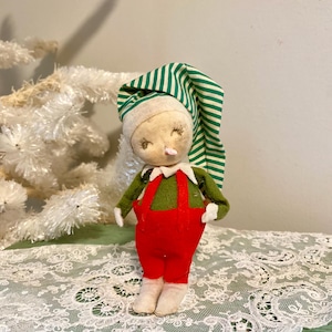 May include: A vintage Christmas elf doll with a green and white striped hat, red pants, and green vest. The doll is made of fabric and has a white face with painted features.