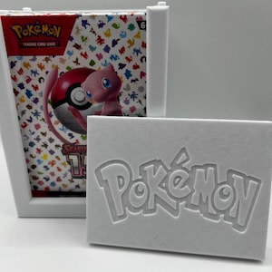 May include: A white, 3D-printed card holder and display case for Pokémon trading cards. The case features the Pokémon logo embossed on the front and a colorful card pack visible inside. The card pack features a Mew and Pokéball graphic.