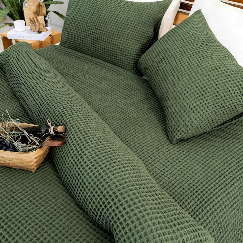 There is a waffle bedspread and pillowcase made of 100% organic cotton on the wooden bed. The bedspread and pillowcase are in forest green colour.