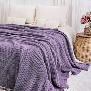 K&ouml;nnte beinhalten: Eine weiche, violette Waffel-Decke mit Fransenrand. Die Decke liegt auf einem Bett mit wei&szlig;en Kissen und einer wei&szlig;en Bettdecke.