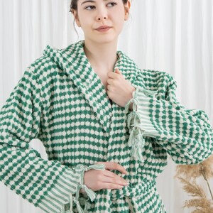 May include: A green and white patterned hooded robe with a matching belt and tassel details. The robe features a textured, dotted design and striped accents on the sleeves. A comfortable and stylish garment.
