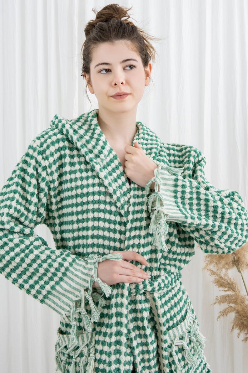 May include: A green and white patterned hooded robe with a matching belt and tassel details. The robe features a textured, dotted design and striped accents on the sleeves. A comfortable and stylish garment.