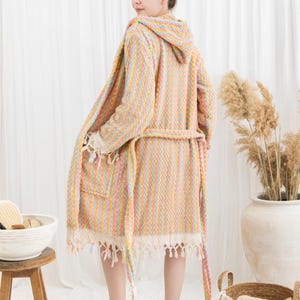 May include: A hooded, pastel-striped robe with a matching belt and fringed edges. The robe is made of a soft, textured fabric and has a pocket on the front. The robe is part of a spa or bath collection.