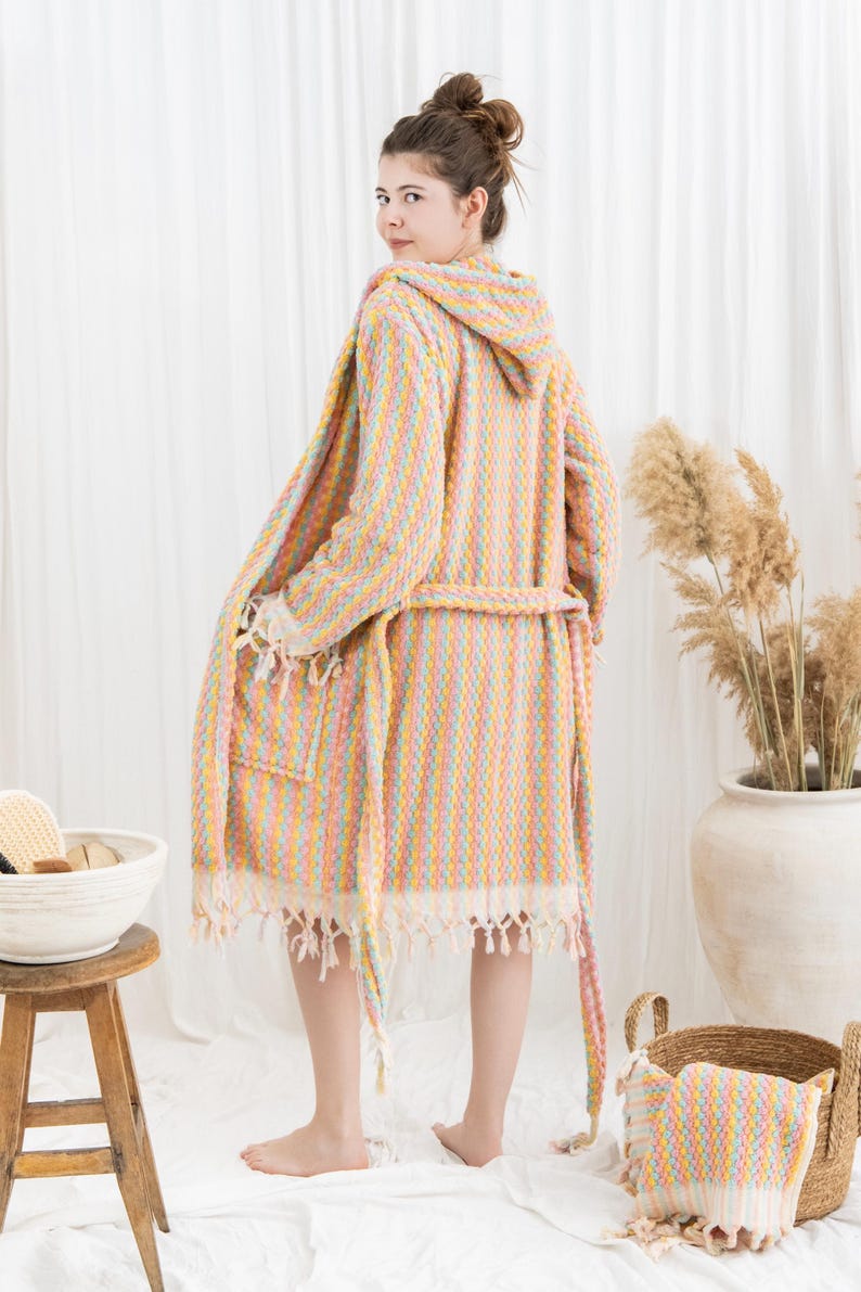 May include: A hooded, pastel-striped robe with a matching belt and fringed edges. The robe is made of a soft, textured fabric and has a pocket on the front. The robe is part of a spa or bath collection.