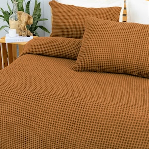 May include: A bed set with a waffle weave pattern in a warm, earthy brown color. The set includes a duvet cover and two pillowcases. The bedding is neatly arranged, suggesting a comfortable and inviting bedroom setting.