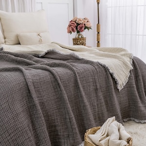 May include: A grey waffle weave throw blanket with a white waffle weave throw blanket underneath. The blankets are on a bed with white pillows and a bouquet of pink roses in a wicker basket.