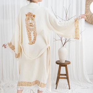 Pode incluir: Robe creme com um desenho de leopardo nas costas. O robe tem um cinto a condizer e acabamento com um padr&atilde;o de pontos. As mangas e a bainha s&atilde;o finalizadas com franjas. O robe &eacute; feito de um tecido macio e leve.