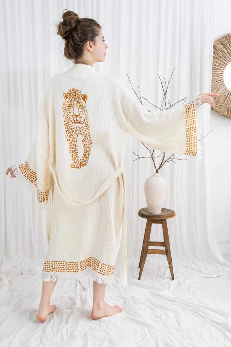 Pode incluir: Robe creme com um desenho de leopardo nas costas. O robe tem um cinto a condizer e acabamento com um padr&atilde;o de pontos. As mangas e a bainha s&atilde;o finalizadas com franjas. O robe &eacute; feito de um tecido macio e leve.