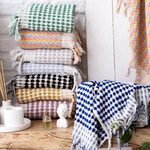 May include: A stack of colourful towels with a blue and white patterned towel in the foreground. The towels have a waffle-like texture and fringe detailing.