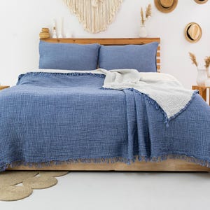 Puede incluir: Una manta de algod&oacute;n azul y blanca con borde de flecos. La manta est&aacute; colocada sobre una cama con fundas de almohada azules.
