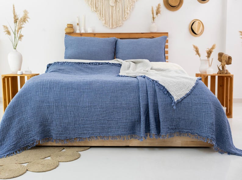 Puede incluir: Una manta de algod&oacute;n azul y blanca con borde de flecos. La manta est&aacute; colocada sobre una cama con fundas de almohada azules.