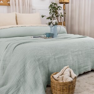 May include: A light green throw blanket with a textured weave, folded on a bed with white pillows. The blanket has a frayed edge.