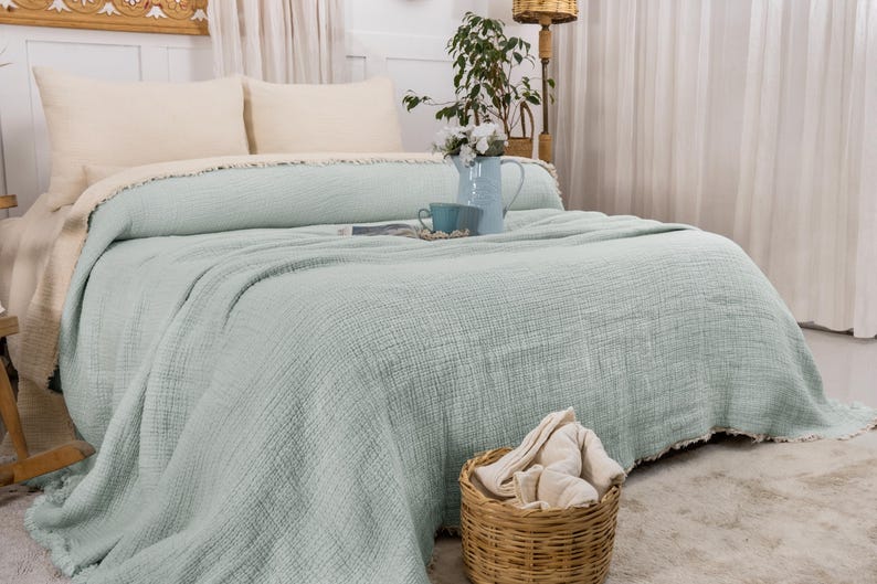 May include: A light green throw blanket with a textured weave, folded on a bed with white pillows. The blanket has a frayed edge.