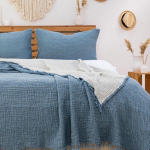 Puede incluir: Una manta de tejido de gofre azul y blanco con flecos en una cama con dos almohadas azules. La cama es de madera y tiene una cabecera.