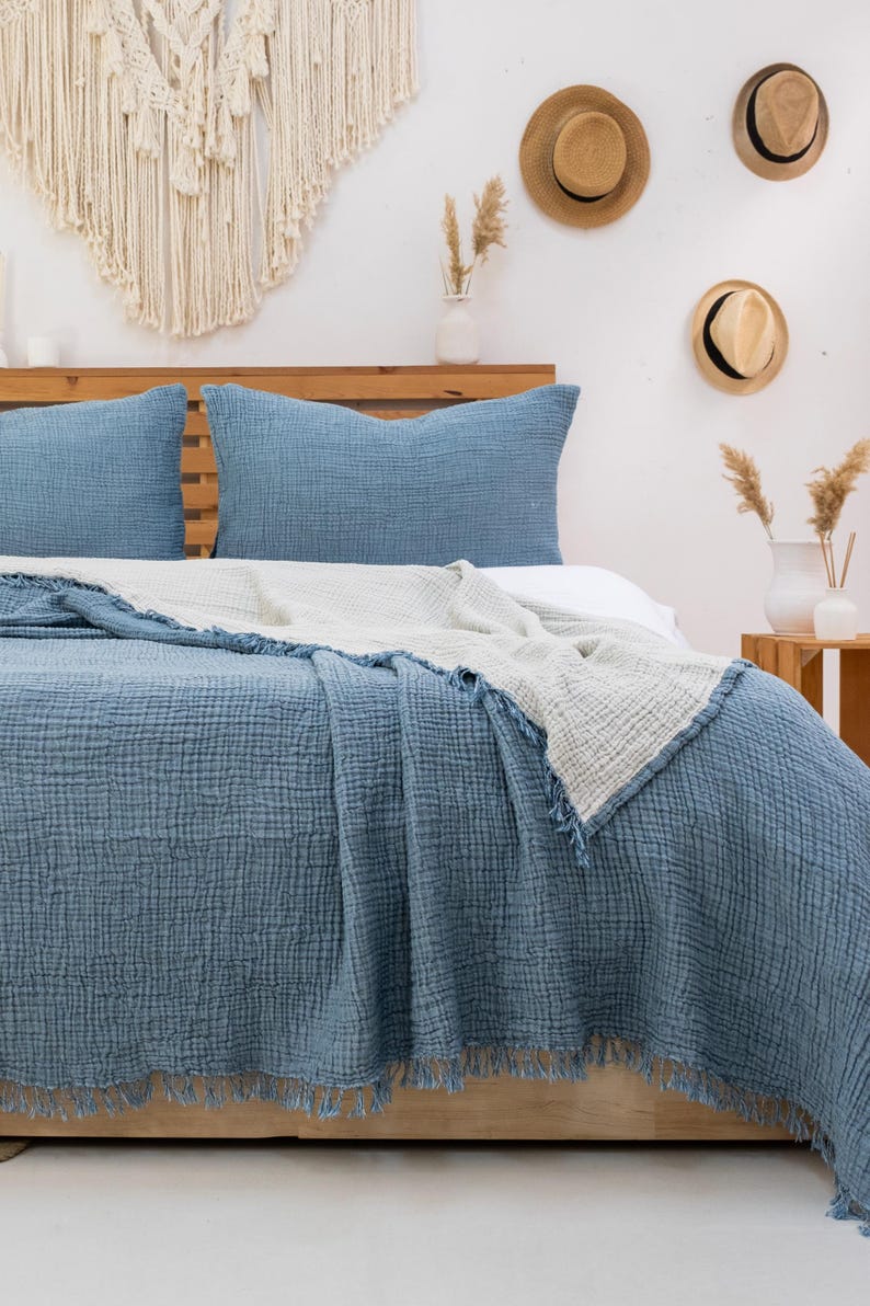 Puede incluir: Una manta de tejido de gofre azul y blanco con flecos en una cama con dos almohadas azules. La cama es de madera y tiene una cabecera.