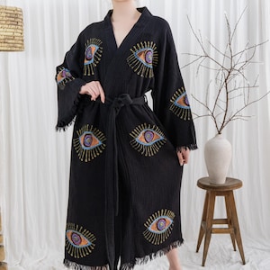 Pode incluir: Robe preta com desenhos de olhos bordados em laranja, azul e roxo. O robe tem uma bainha com franjas e um cinto a condizer. As mangas s&atilde;o compridas e largas, e o robe &eacute; feito de um tecido macio e texturizado.