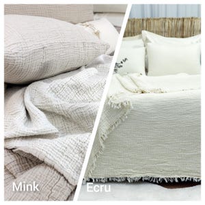 May include: Two bedding sets are displayed, one in mink and the other in ecru. The mink set includes a pillow and a blanket with a textured, crinkled appearance. The ecru set features a blanket with a fringed edge and pillows, all on a bed.