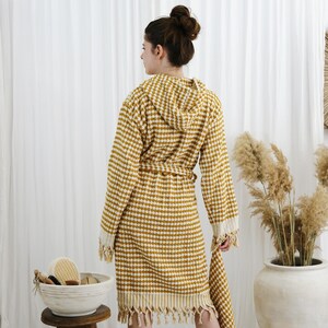 May include: Mustard yellow and white checkered hooded bathrobe with a matching belt and fringed edges. The robe is made of a soft, textured fabric. The robe is a comfortable and stylish choice for lounging or after a shower.