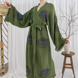 Pode incluir: Robe verde-oliva com decote em V, mangas compridas e cinto a condizer. O robe apresenta um design de olho em azul, laranja e roxo. As mangas t&ecirc;m uma borda com franjas. O robe &eacute; feito de tecido leve.