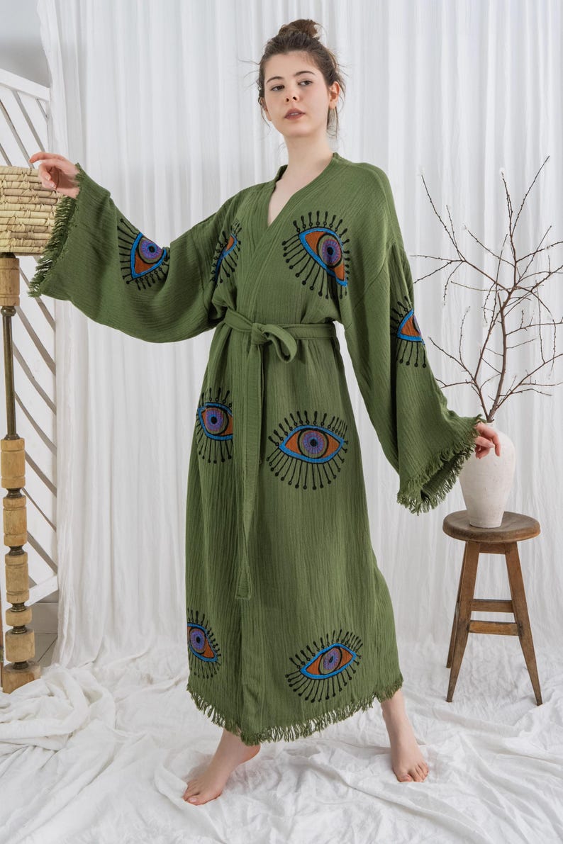 Pode incluir: Robe verde-oliva com decote em V, mangas compridas e cinto a condizer. O robe apresenta um design de olho em azul, laranja e roxo. As mangas t&ecirc;m uma borda com franjas. O robe &eacute; feito de tecido leve.