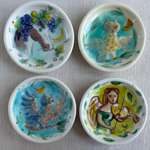 May include: Set of four ceramic dishes with colourful painted designs. Each dish features a different animal: a horse, an owl, a bird, and an angel. The dishes are perfect for serving snacks or appetizers.
