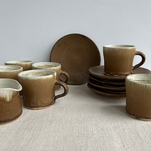 Könnte beinhalten: Ein Set aus braunen und weißen Kaffeetassen und Untertassen aus Keramik. Die Tassen haben einen weißen Rand und eine braune Glasur. Die Untertassen sind braun und haben einen leicht erhöhten Rand.