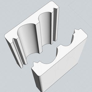 Puede incluir: Un molde de plástico blanco con dos piezas separadas, cada una con dos cavidades cilíndricas. El molde está diseñado para crear objetos con forma redondeada.