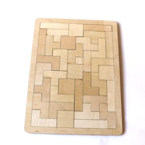 May include: Wooden puzzle featuring interlocking geometric shapes. The puzzle is made of light-coloured wood and has various rectangular and L-shaped pieces. The pieces fit together to form a larger rectangular shape. The puzzle is designed for problem-solving and spatial reasoning.