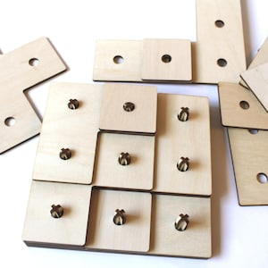 May include: Wooden puzzle pieces in various shapes and sizes. The pieces are light brown with small, dark brown pegs and holes. Some pieces are square, while others are rectangular or L-shaped. The puzzle is designed for children.